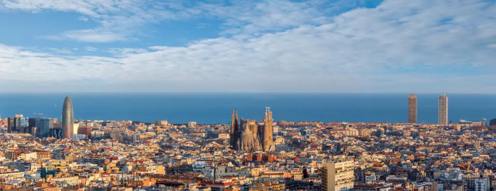 Panoramic view of Barcelona skyline with Sagrada Familia, modern skyscrapers, and the Mediterranean Sea.